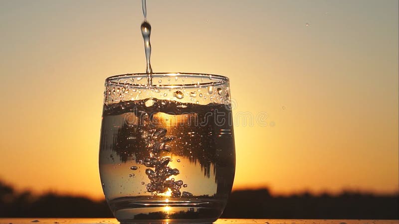 Vetro di riempimento con acqua al tramonto, movimento lento