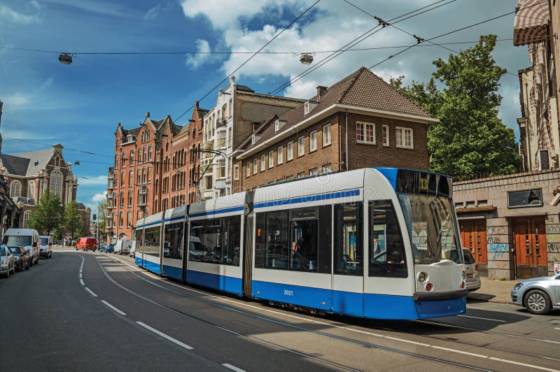 Via con cielo blu, vecchie costruzioni ed il tram passanti vicino a Amsterdam immagine stock