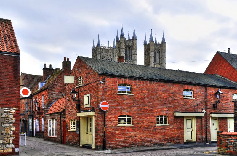 Attractive historic red-brick houses and cobbled streets in the neighborhood of Lincoln Cathedral, England. Cathedral towers in the background. Attractive historic red-brick houses and cobbled streets in the neighborhood of Lincoln Cathedral, England. Cathedral towers in the background.