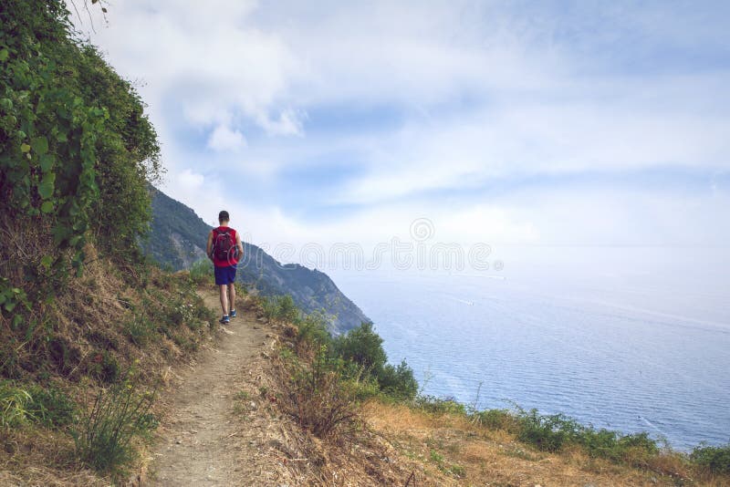 A hiker on a narrow path in the Ligurian mountains in national park Cinque Terre  Italy. The Mediterranean sea below. A hiker on a narrow path in the Ligurian mountains in national park Cinque Terre  Italy. The Mediterranean sea below.