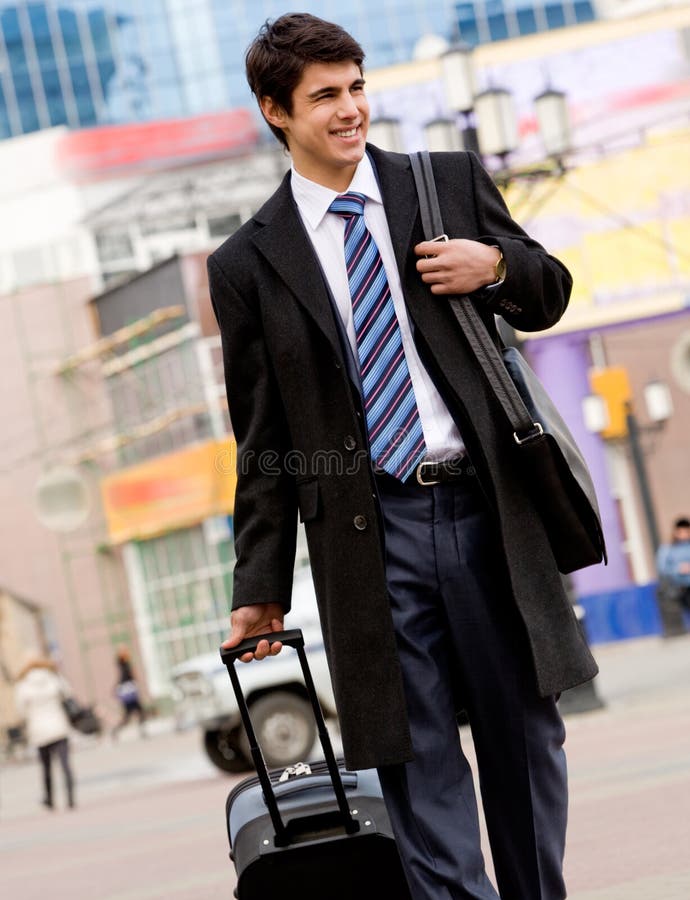 Image of happy guy in suit and coat walking with his baggage and bag. Image of happy guy in suit and coat walking with his baggage and bag