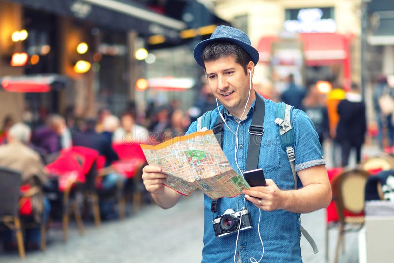 Viaggiatore con lo sguardo d'avanguardia facendo uso della mappa sulla via in pieno dei ristoranti e dei negozi della città europ fotografia stock libera da diritti Viaggiatore con lo sguardo d'avanguardia facendo uso della mappa sulla via in pieno dei ristoranti e dei negozi della città europ fotografia stock libera da diritti