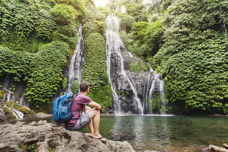 Viaggiatore con zaino e sacco a pelo che esamina cascata in Bali, turismo immagini stock Viaggiatore con zaino e sacco a pelo che esamina cascata in Bali, turismo immagini stock