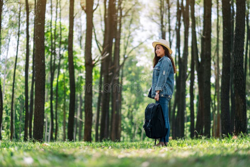 Viaggiatore femminile con un cappello e uno zaino che esamina legno il bello di pino fotografie stock Viaggiatore femminile con un cappello e uno zaino che esamina legno il bello di pino fotografie stock