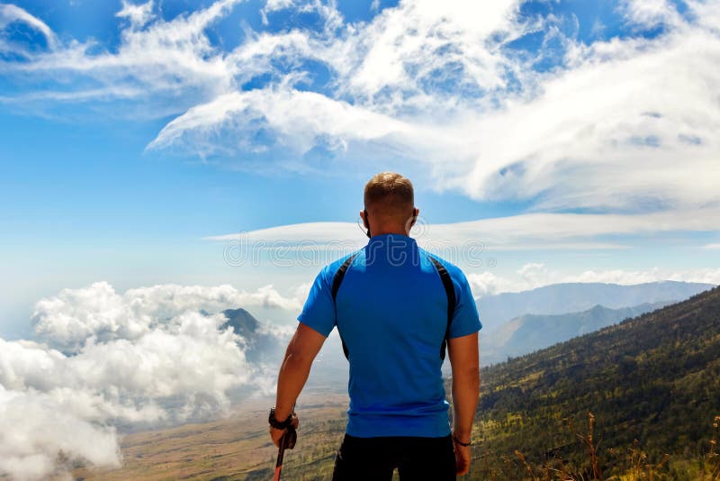 Viaggiatore sportivo del tipo in una maglietta blu su un fondo di bello cielo con le nuvole nelle montagne fotografia stock Viaggiatore sportivo del tipo in una maglietta blu su un fondo di bello cielo con le nuvole nelle montagne fotografia stock