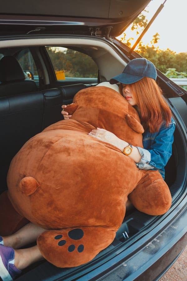 Viajante da mulher que encontra-se para baixo no carro do carro com porta traseira e que abraça uma Big Bear fotos de stock royalty free Viajante da mulher que encontra-se para baixo no carro do carro com porta traseira e que abraça uma Big Bear fotos de stock royalty free