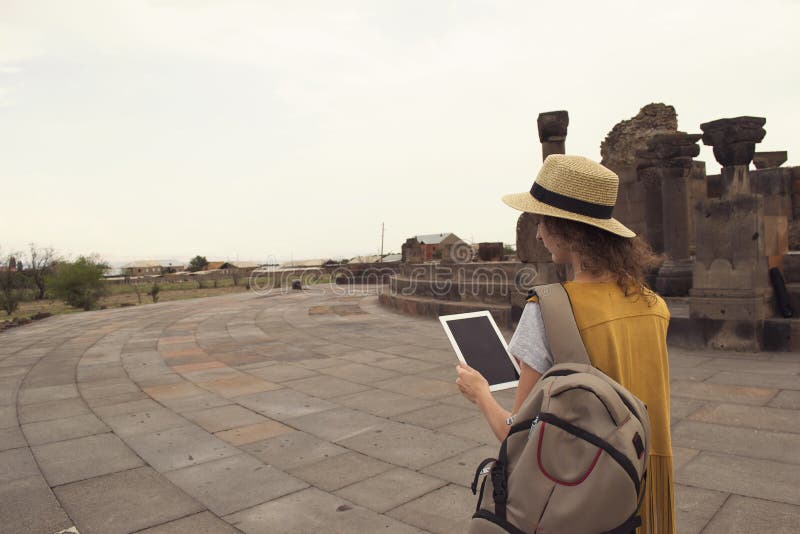 Viajero femenino con la tableta de la tenencia de la mochila durante visitar Zvartnots Armenia Tecnología y el viajar entonado fotos de archivo libres de regalías Viajero femenino con la tableta de la tenencia de la mochila durante visitar Zvartnots Armenia Tecnología y el viajar entonado fotos de archivo libres de regalías