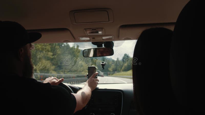 Viajero pareja conducir coche en vacaciones siguiendo la navegación en el smartphone. el macho alcanza su mano y entra en el túnel