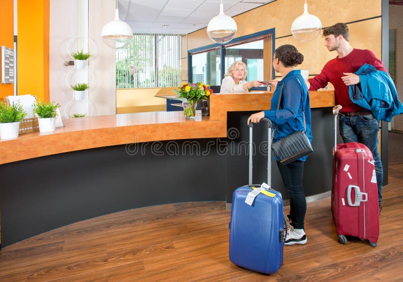 Young couple at the check in counter of a hotel, having just arrived with their luggage from the airport. Young couple at the check in counter of a hotel, having just arrived with their luggage from the airport