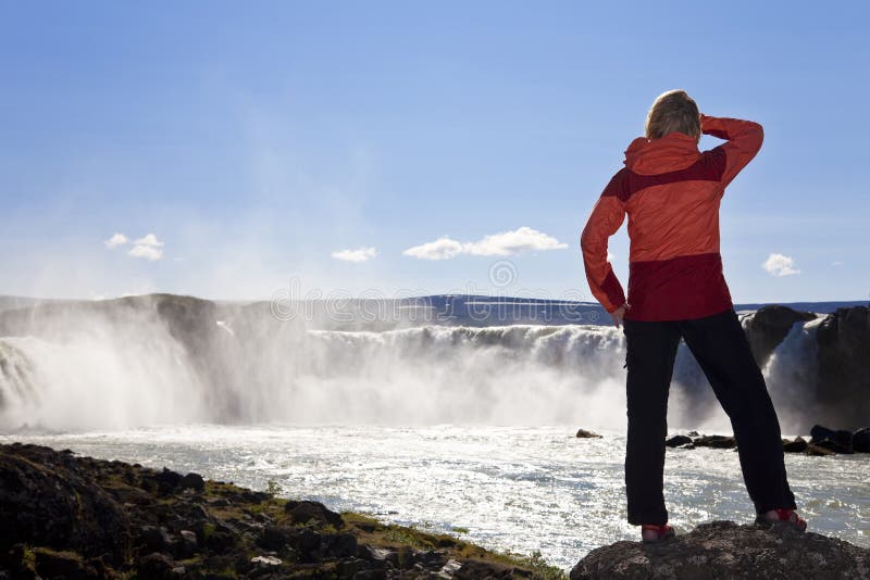 Viandante che si leva in piedi ad una cascata, Islanda della donna fotografie stock libere da diritti Viandante che si leva in piedi ad una cascata, Islanda della donna fotografie stock libere da diritti