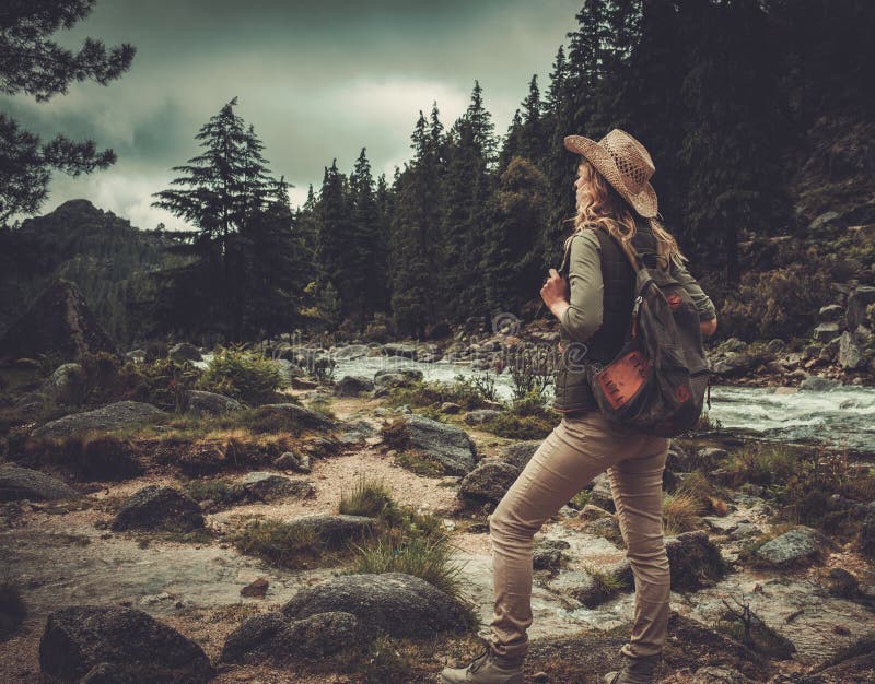 Viandante della donna che sta vicino al fiume selvaggio della montagna immagini stock Viandante della donna che sta vicino al fiume selvaggio della montagna immagini stock