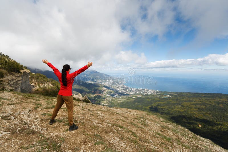Viandante incoraggiante della donna a braccia aperte al picco di montagna, alle mani di diffusione della ragazza con gioia ed all immagine stock libera da diritti Viandante incoraggiante della donna a braccia aperte al picco di montagna, alle mani di diffusione della ragazza con gioia ed all immagine stock libera da diritti