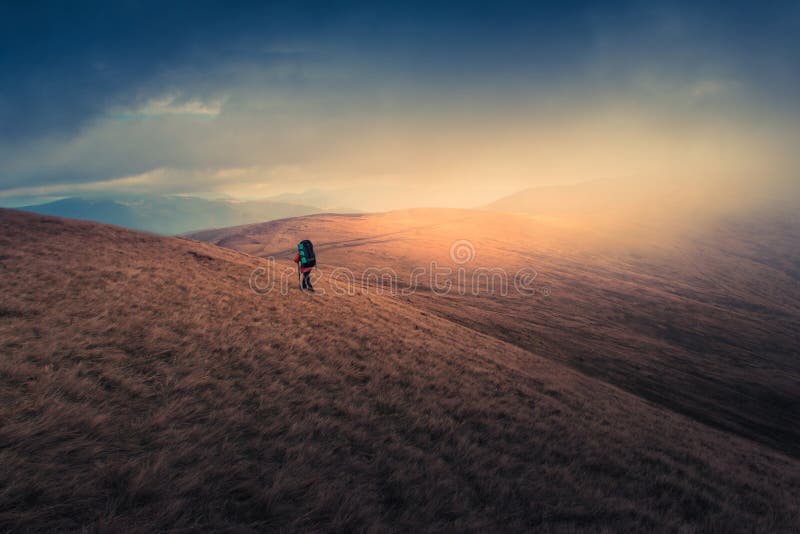 Viandante sola con lo zaino che cammina lungo la pista sulla cima della montagna al tempo nebbioso di giorno immagine stock Viandante sola con lo zaino che cammina lungo la pista sulla cima della montagna al tempo nebbioso di giorno immagine stock
