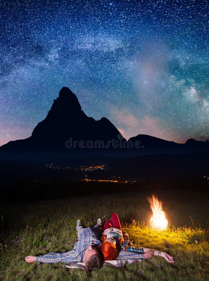 Viandanti felici delle coppie che ammirano le stelle luminose e che si trovano vicino al fuoco alla notte Esposizione lunga fotografie stock libere da diritti Viandanti felici delle coppie che ammirano le stelle luminose e che si trovano vicino al fuoco alla notte Esposizione lunga fotografie stock libere da diritti
