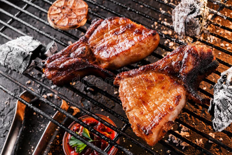 Viande grillée de bifteck à l'os avec l'ail au-dessus des charbons sur un barbecue, fond foncé avec la lumière du feu Vue sup?rie photos libres de droits Viande grillée de bifteck à l'os avec l'ail au-dessus des charbons sur un barbecue, fond foncé avec la lumière du feu Vue sup?rie photos libres de droits