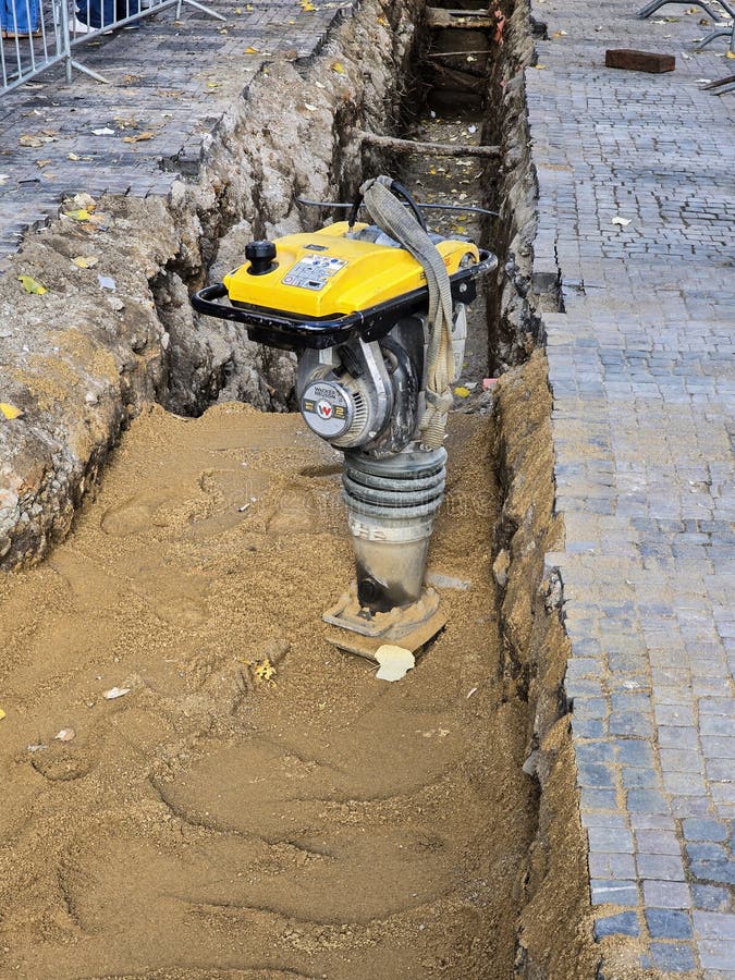 A vibratory rammer compacts sand in a trench during road works. royalty free stock images