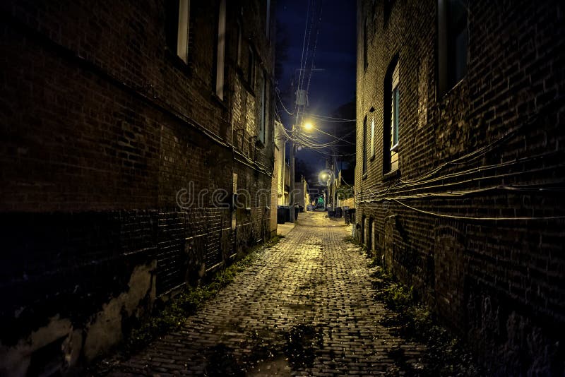 Vicolo urbano scuro e sinistro del mattone del ciottolo della città alla notte