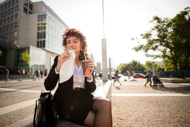 Vida de la prisa - mujer de negocios que come en calle imagen de archivo Vida de la prisa - mujer de negocios que come en calle imagen de archivo