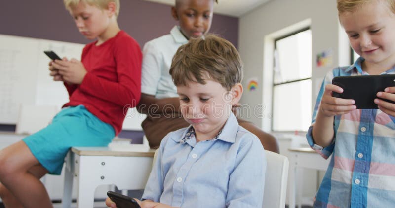 Video of diverse boys sitting at school desks and playing games on smartphones