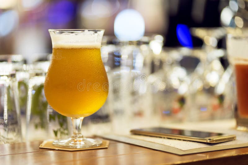 Vidro da cerveja clara com o telefone esperto no contador da barra no clube noturno fotos de stock Vidro da cerveja clara com o telefone esperto no contador da barra no clube noturno fotos de stock