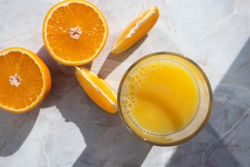 Vidro de sumo de laranja fresco e laranjas cortadas em mesa clara foto de stock Vidro de sumo de laranja fresco e laranjas cortadas em mesa clara foto de stock