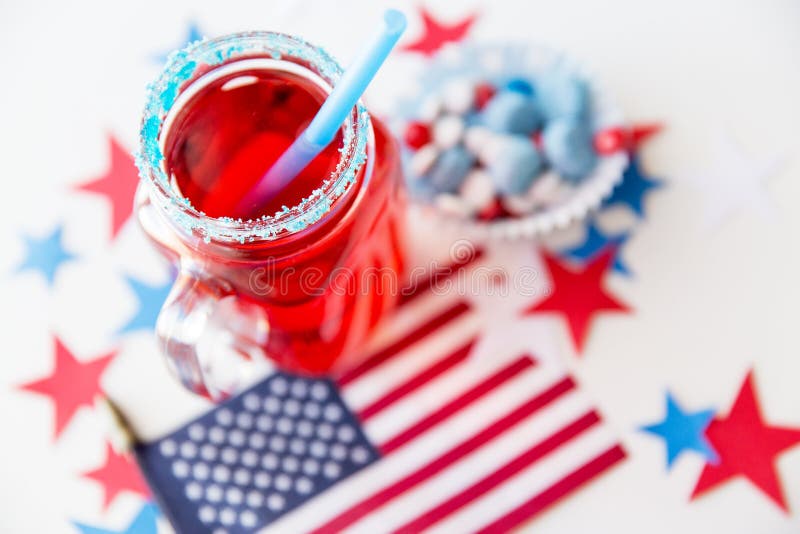 American independence day, celebration, patriotism and holidays concept - close up of juice glass, flag and candies at 4th july party. American independence day, celebration, patriotism and holidays concept - close up of juice glass, flag and candies at 4th july party