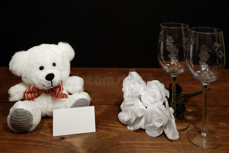 Vidros de vinho gravados bonitos com rosas brancas e o urso de peluche branco e etiqueta do nome na tabela de madeira e no fundo imagens de stock Vidros de vinho gravados bonitos com rosas brancas e o urso de peluche branco e etiqueta do nome na tabela de madeira e no fundo imagens de stock