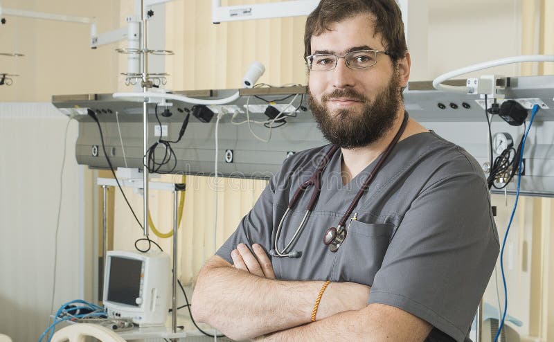 Vidros vestindo do doutor farpado e trabalhos cinzentos de uma veste com equipamento do hospital imagem de stock Vidros vestindo do doutor farpado e trabalhos cinzentos de uma veste com equipamento do hospital imagem de stock