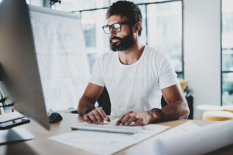 Vidros vestindo do olho do homem farpado pensativo e trabalho no estúdio-escritório moderno do sótão Fundo borrado horizontal imagens de stock Vidros vestindo do olho do homem farpado pensativo e trabalho no estúdio-escritório moderno do sótão Fundo borrado horizontal imagens de stock