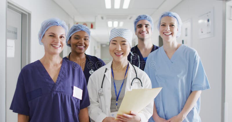 Vidéo d'un groupe diversifié de travailleurs médicaux heureux dans des casquettes chirurgicales souriant dans le couloir de l'hôpi banque de vidéos