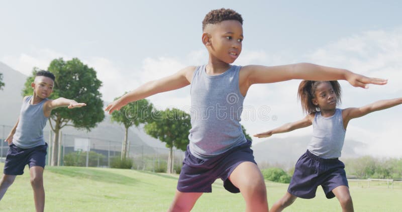Vidéo de trois écoliers afro-américains pratiquant le yoga debout en classe extérieure banque de vidéos