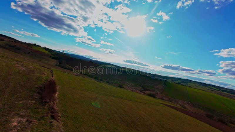 Vidéo verticale FPV drone vue banque sur des champs verts vibrants et campagne ondulante sous ciel bleu vif avec clips vidéos