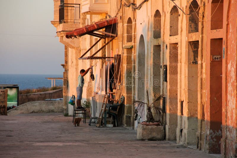 Vie réelle de côté de mer de Malte pendant le coucher du soleil orange - vêtements accrochants de garçon séchant, deux machines à images stock Vie réelle de côté de mer de Malte pendant le coucher du soleil orange - vêtements accrochants de garçon séchant, deux machines à images stock