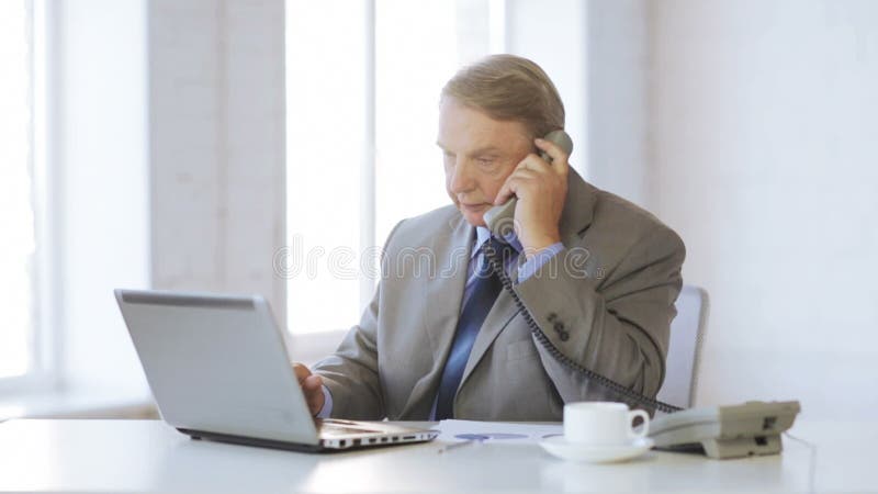 Vieil homme avec l'ordinateur portable prenant un appel téléphonique