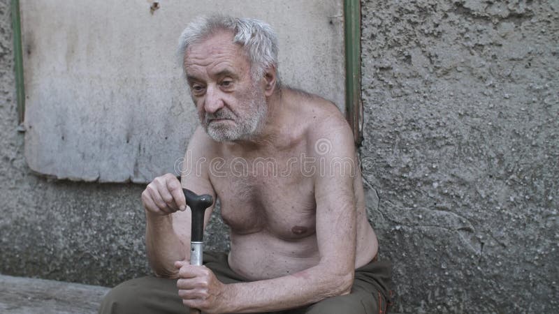 Vieil homme triste de mendiant avec une canne se reposant sur la rue