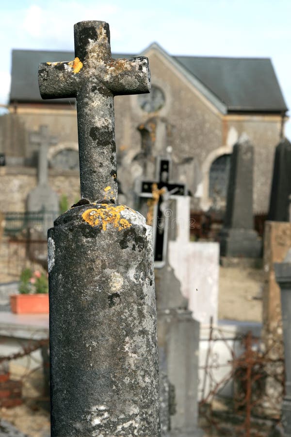 An old stone cross at the churchyard of Dun-sur-Meuse in the northern part of France. At the background a chaos of leaning crosses and a part of the church. An old stone cross at the churchyard of Dun-sur-Meuse in the northern part of France. At the background a chaos of leaning crosses and a part of the church.