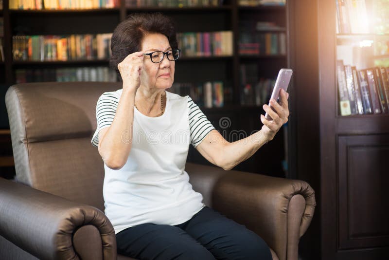 Vieja mujer asiática que mira la pantalla del smartphone imagen de archivo libre de regalías Vieja mujer asiática que mira la pantalla del smartphone imagen de archivo libre de regalías