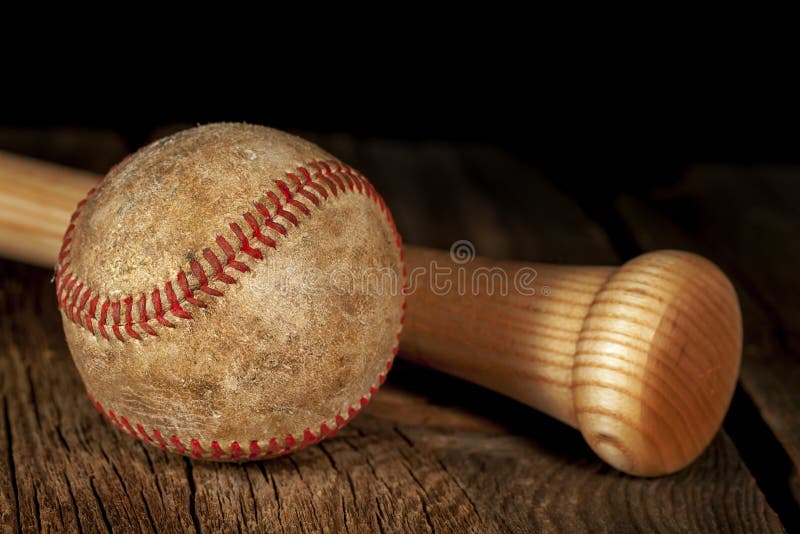 An old worn baseball and wood bat on wood surface with black background. An old worn baseball and wood bat on wood surface with black background