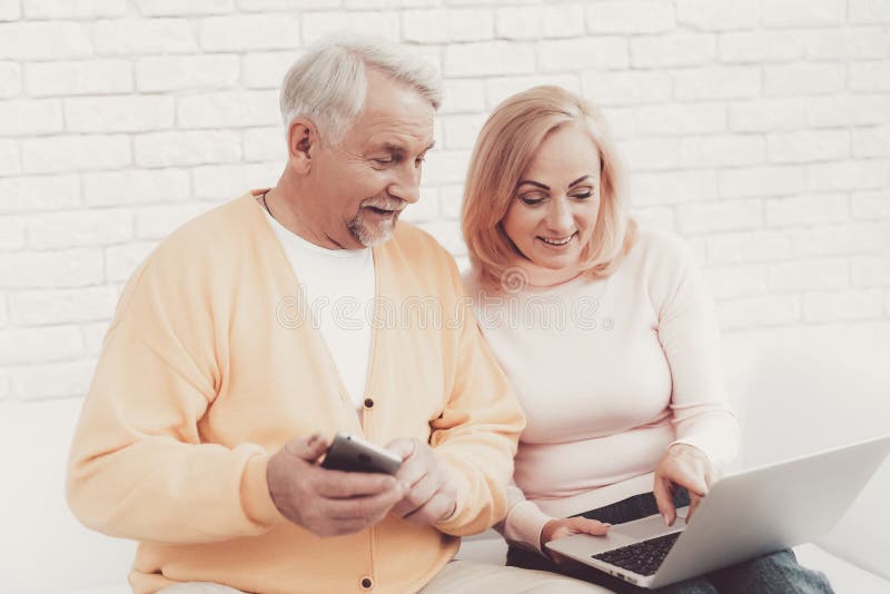 Viejo hombre cerca de la mujer mayor con Smartphone y el ordenador portátil imagen de archivo
