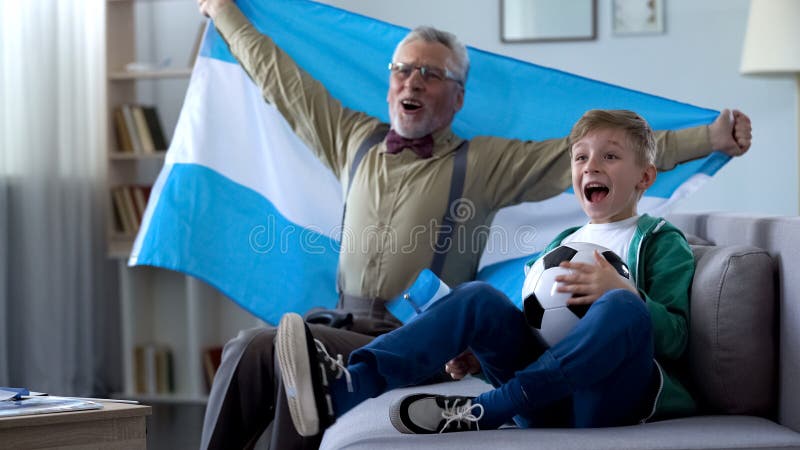 Viejo hombre emocionado y niño pequeño que celebran la victoria del equipo de fútbol de la Argentina imágenes de archivo libres de regalías Viejo hombre emocionado y niño pequeño que celebran la victoria del equipo de fútbol de la Argentina imágenes de archivo libres de regalías