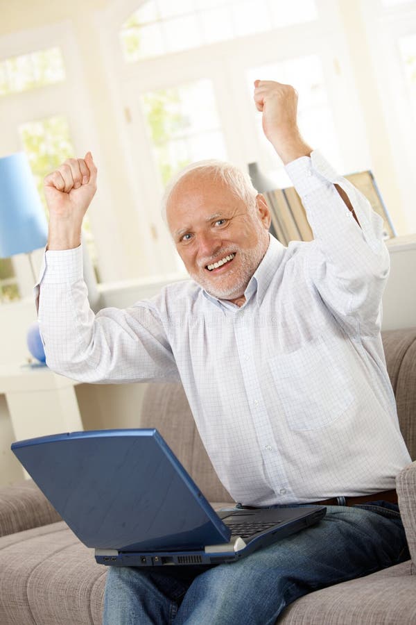 Viejo hombre feliz que se sienta en el sofá con la computadora portátil