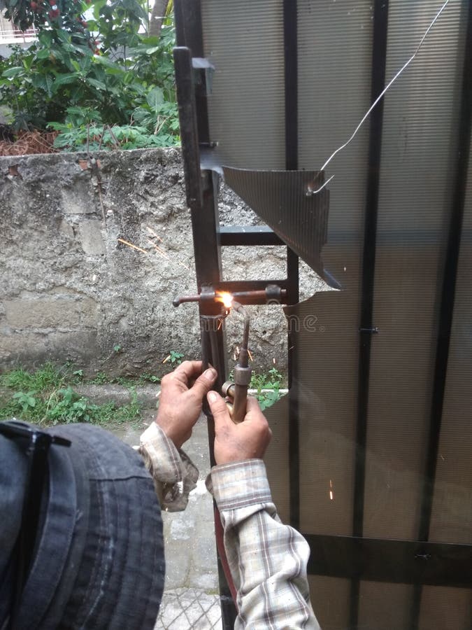 Viejo hombre que suelda con autógena una manija negra corrosiva del hierro de la puerta imagen de archivo libre de regalías Viejo hombre que suelda con autógena una manija negra corrosiva del hierro de la puerta imagen de archivo libre de regalías