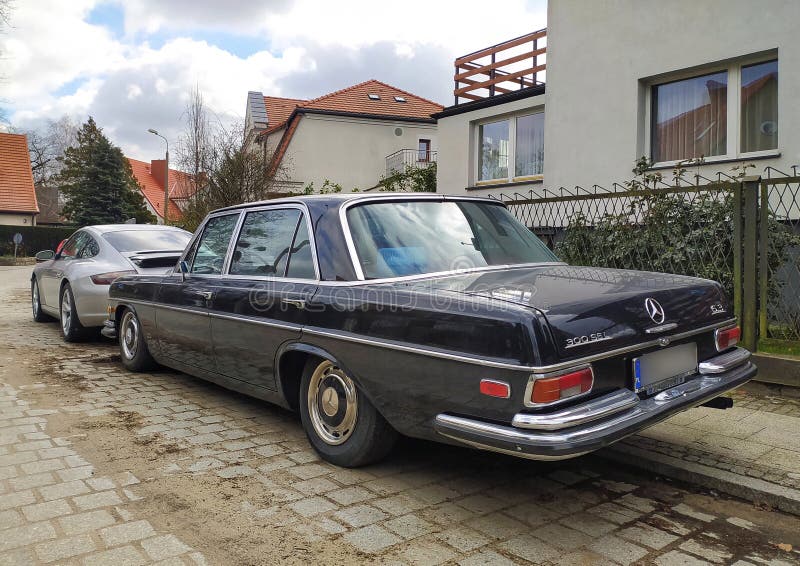 Old vintage classic black extremely rare veteran luxury historic model of black chromed luxury performance sports sedan muscle car Mercedes Benz 300 SEL 6.3 lite V8 engine parked in old district in Gdansk Wrzeszcz in northern Poland. Old apartment houses and huge trees in the background. Left side and rear part view with logo. Modern Porsche carrera parked in front of this sports four-door automobile. Produced between 1968 and 1972. March 24th, 2024. Old vintage classic black extremely rare veteran luxury historic model of black chromed luxury performance sports sedan muscle car Mercedes Benz 300 SEL 6.3 lite V8 engine parked in old district in Gdansk Wrzeszcz in northern Poland. Old apartment houses and huge trees in the background. Left side and rear part view with logo. Modern Porsche carrera parked in front of this sports four-door automobile. Produced between 1968 and 1972. March 24th, 2024.