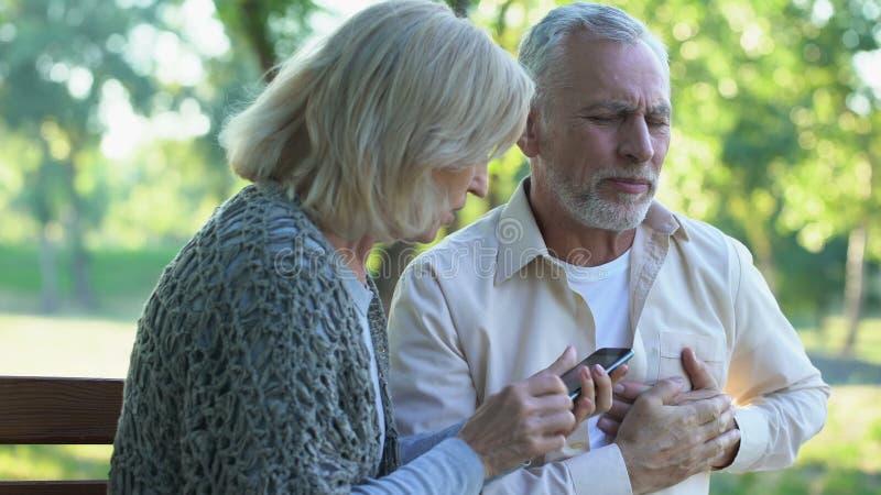 Viejos pares que se sientan en banco, arritmia sufridora del hombre, esposa que llama emergencia