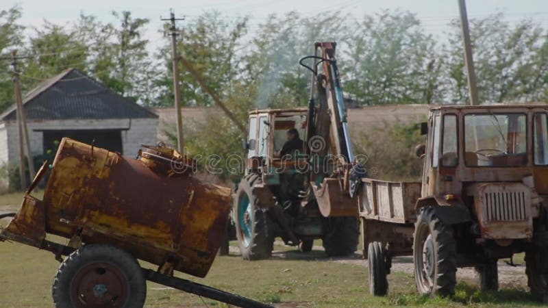 Viendo hacia atrás el granjero hombre de edad avanzada conduce a un tractor agrícola a través de su granja y empieza a trabajar