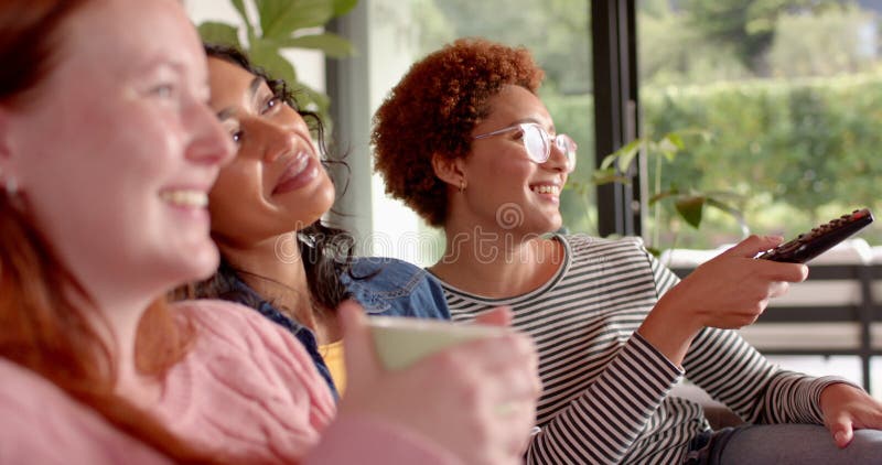 Viendo la televisión y relajando a las diversas amigas disfrutando del tiempo juntos en el sofá almacen de video