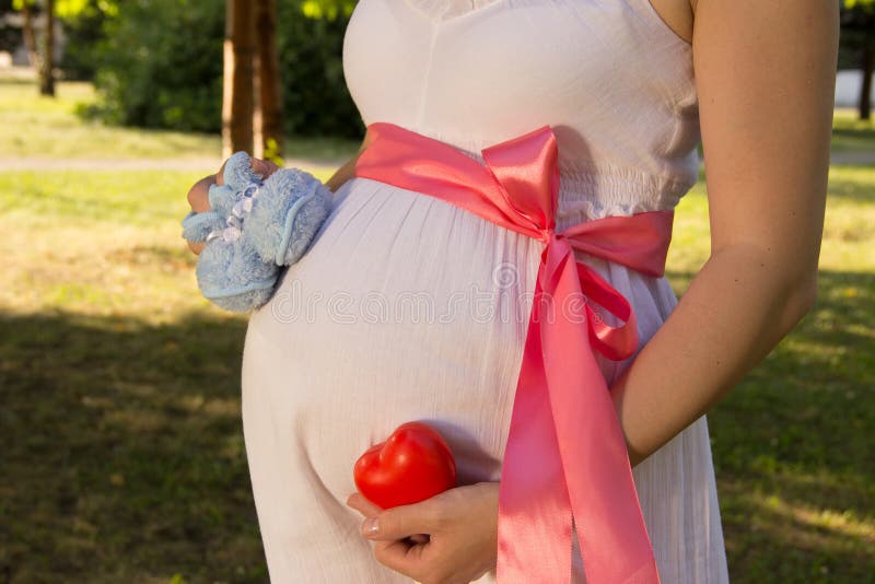Vientre de la muchacha embarazada en el vestido blanco del verano en parque con el bootie fotos de archivo libres de regalías Vientre de la muchacha embarazada en el vestido blanco del verano en parque con el bootie fotos de archivo libres de regalías