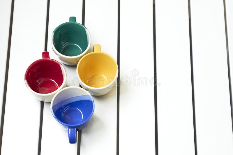 a small bowl-shaped container for drinking from, typically having a handle.Four cups on a white striped table. a small bowl-shaped container for drinking from, typically having a handle.Four cups on a white striped table.