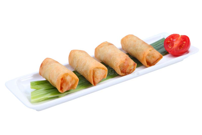 Four fried Chinese spring rolls in a row on a white, long, narrow porcelain plate, decorated with a stalk of green onion and half a tomato, isolated on white background. Four fried Chinese spring rolls in a row on a white, long, narrow porcelain plate, decorated with a stalk of green onion and half a tomato, isolated on white background.