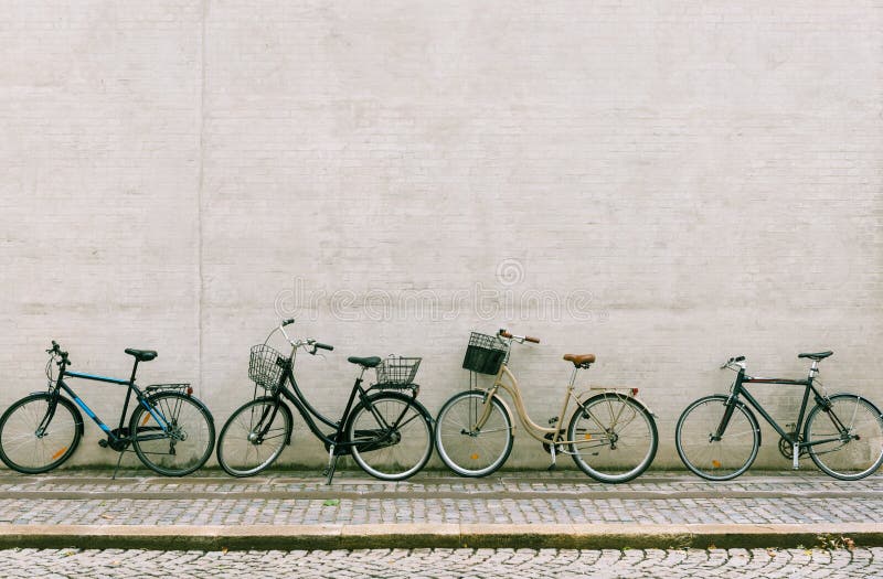Four bicycles stand near a white brick wall. Several different bikes parked along an empty street in Copenhagen. Four bicycles stand near a white brick wall. Several different bikes parked along an empty street in Copenhagen